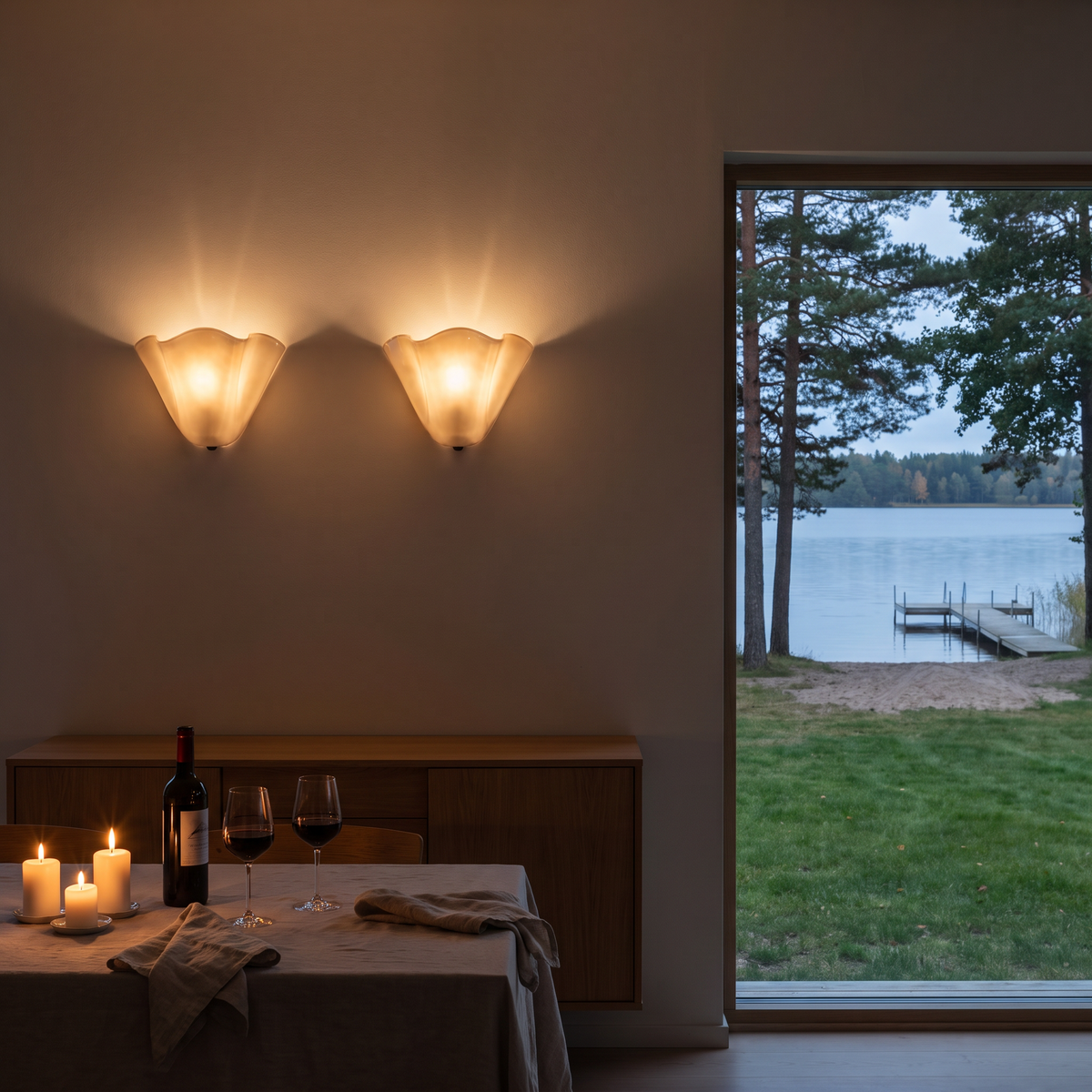 Pair of sculpted glass flower wall sconces lit above a candlelit dinner table for two in a lake house at dusk