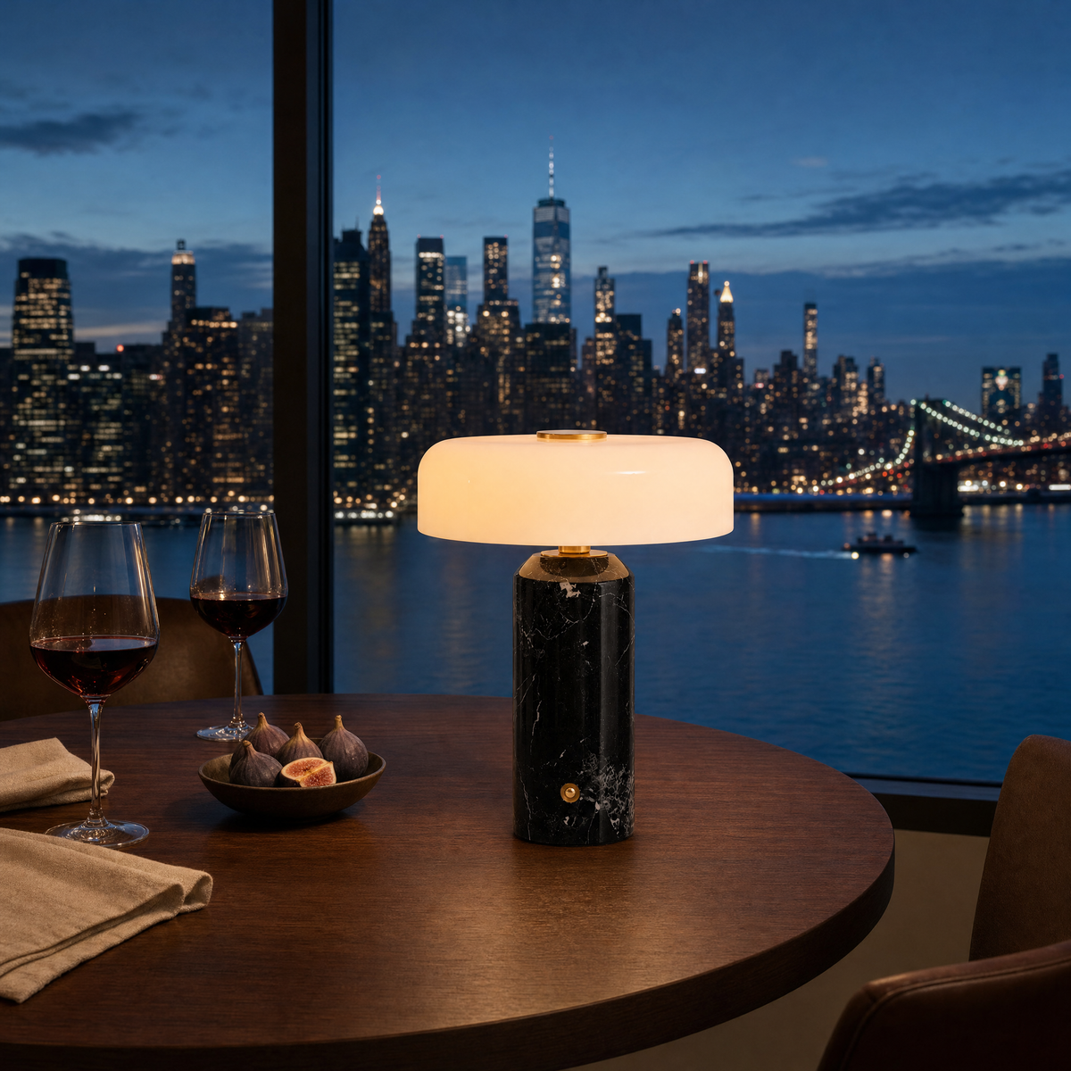 Cordless black Nero Marquina marble table lamp lit on a dining table set for two, Manhattan skyline at dusk